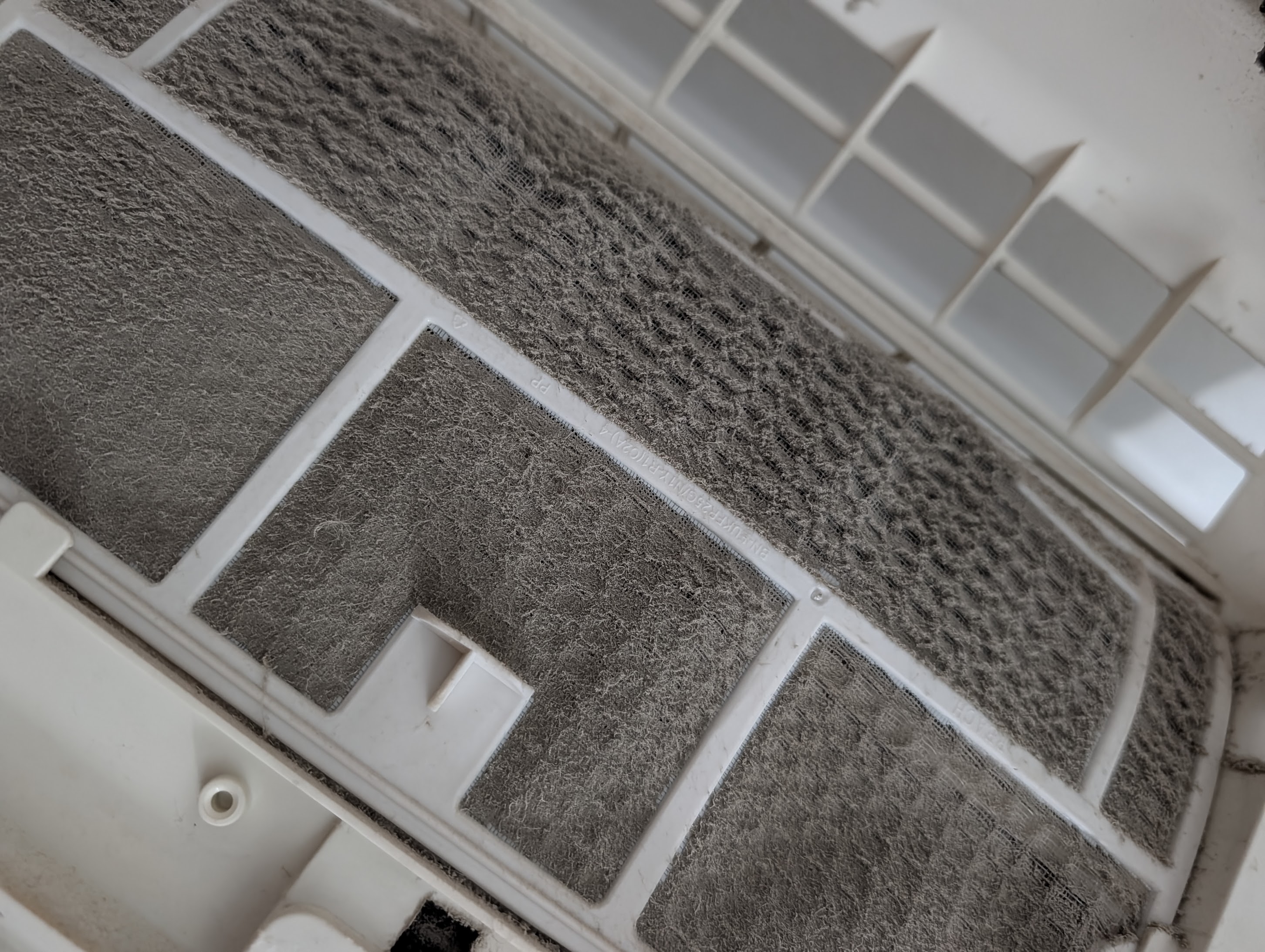 Air-conditioning filter almost entirely occluded by a thick grey mat of dust and lint
